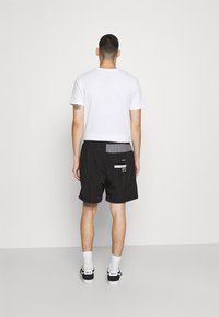 Shorts noirs avec un panneau gris et du texte blanc sur la poche arrière, associés à un t-shirt blanc uni et des baskets noires.
