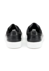Sneaker in pelle nera con una texture liscia, suole in gomma bianca e un inserto posteriore per la presa. Design minimalista con profilo basso.