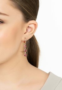 Gli orecchini a goccia in oro rosa presentano tre pietre rosa a forma di lacrima. Il design mette in risalto catene delicate e una finitura lucida.