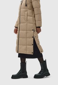 Kreminio ilgo pūkinio paltuko su siuvinėta raštu, šoninėmis kišenėmis ir juodais akcentais. Dėvimas su juodais kulkšnies auliniais batais, tekstūruotu padu ir lengvai užsitempiamu dizainu.