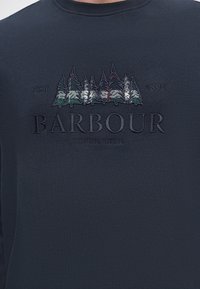 Sweat-shirt bleu marine foncé avec des pins brodés, les textes "EST 1894", "BARBOUR" et "SOUTH SHIELDS" sur la poitrine.