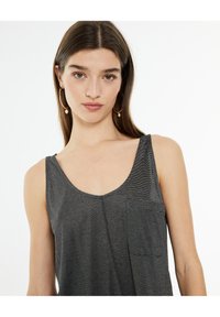 Top sin mangas a rayas grises con escote redondeado y un bolsillo en el pecho. La tela parece ligera y suave, adecuada para un uso informal.