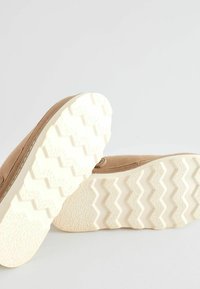 Brown suede shoes with a white zigzag patterned sole. Features a simple design with rounded edges and minimal stitching.