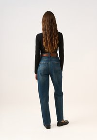 TMavě modré džíny s vysokým pasem a volným střihem, s dvěma zadními kapsami a hnědým koženým opaskem. Tkanina je denim s hladkou texturou.