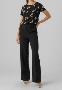 Blusa negra con estampado floral y mangas cortas, combinada con pantalones negros de cintura alta. Tejido suave, diseño de pierna ancha y sandalias planas.