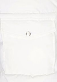 Poche en tissu blanc avec rabat maintenu par un seul bouton rond argenté, cousue sur un fond blanc assorti.