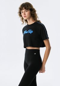 Zwarte cropped t-shirt met blauwe gestructureerde "Rise Up" letters en zijkanten. Gecombineerd met hoge zwarte leggings.