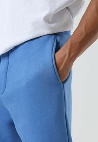 Blauwe katoenen joggingbroek met een gladde textuur, voorzien van zijzakken en een ontspannen pasvorm, gecombineerd met een wit T-shirt.