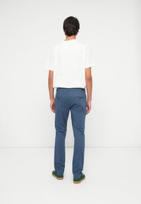 Blue cotton pants with a relaxed fit, flat front, and rear pockets, paired with a plain white t-shirt and green casual shoes.