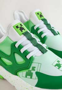 Paar weiße und grüne Turnschuhe mit pixeligen Videospielcharakter-Logos auf der Zunge und den Seiten, weißen Schnürsenkeln und grünen Akzenten.