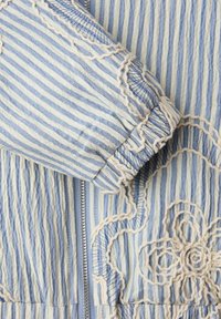 Blåt og hvidt stribet stof med lynlås, med cremefarvet forhøjet blomsterbroderi og elastiske manchetter.