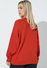 Felpa rossa over-size con maniche lunghe, polsini a coste e scollo rotondo. Realizzata in un tessuto morbido, presenta una superficie liscia.