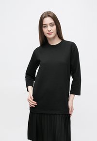 Czarna koszula z długim rękawem wykonana z bawełny, z okrągłym dekoltem, luźnym krojem i gładką fakturą. Posiada prosty dół i boczne rozcięcia.