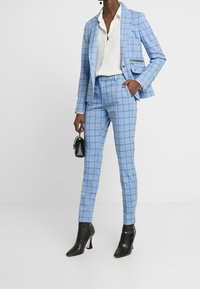 Light blue checkered suit with a tailored blazer and fitted pants, paired with a white shirt and black ankle boots. Small black handbag included.