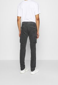 Szare spodnie cargo z bocznymi kieszeniami i luźnym krojem, zestawione z białą koszulką i białymi trampkami. Widoczne przeszycia i miękka tekstura.