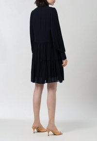 Mustat kerrokselliset mekko pitkillä hihoilla, kevyttä kangasta ja korkea kaula-aukko. Yhdistetty nude-värisiin korkokenkiin, joissa on kerrostettu helma.