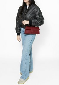 Giubbotto bomber in pelle nera, jeans a zampa d'elefante azzurri chiari e una borsa bordeaux. Sneakers con una finitura testurizzata completano l'outfit.