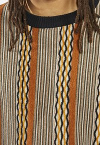 Patterned sweater featuring vertical stripes in brown, white, green, and orange with a textured, ribbed design and a black neckline.