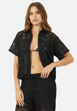 Zwarte haakshirt met korte mouwen, met een geometrisch patroon en knopen. Draag het over een bikini, gecombineerd met een bijpassende broek.