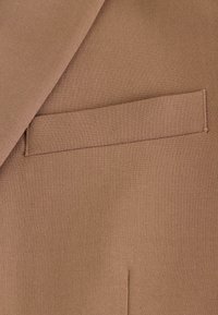 Un tejido marrón con una textura suave presenta un bolsillo para entradas delgado, alineado verticalmente, con una costura prolija a lo largo de los bordes.