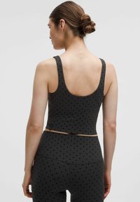 Čierna športová podprsenka s bodkovaným vzorom, s širokými ramienkami a skráteným strihom, v kombinácii s vysokými legínami v rovnakom dizajne.