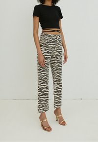 Czarny prążkowany krótki top z krótkimi rękawami, zestawiony z beżowymi spodniami z czarnym falistym wzorem zebry oraz złotymi sandałami na obcasie.