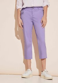 Fioletowe spodnie capri o gładkiej fakturze, z przednimi kieszeniami i suwakiem z boku. Połączone z białymi trampkami.