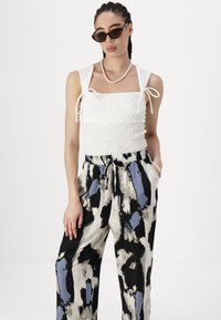 White smocked crop top with tie straps paired with black, cream, and blue abstract patterned trousers. Features a relaxed fit and pockets.