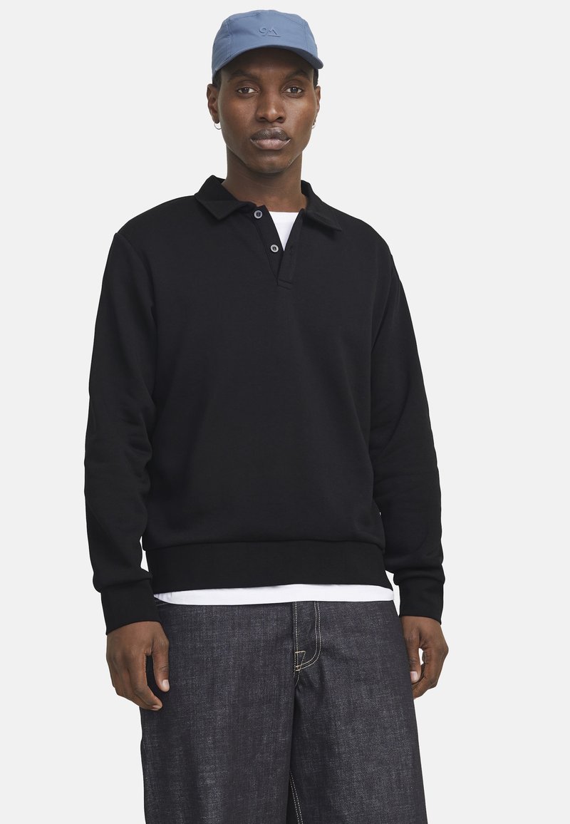 Sort langærmet polo sweatshirt med to-knaps krave, parret med mørk denim bukser og en lys blå kasket. Simpelt design, klassisk pasform.