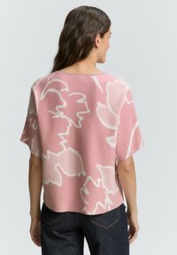 Růžový pletený svetr s bílými květinovými vzory, krátké rukávy a volný střih. Disponuje kulatým výstřihem a lehce zkráceným lemem.