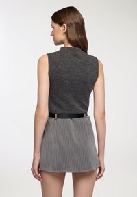 Top grigio senza maniche con collo alto, abbinato a una minigonna grigia a righe sottili, con cintura nera. Materiali semplici e strutturati.