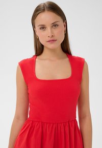 Punane kleit ribakujulise tekstuuriga rinnaosas ja sujuva, voolava seeliku osaga. Ruudukujuline kaelus ja lühikesed varrukad täiustavad selle disaini.