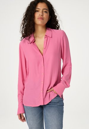 Rosa langärmlige Bluse mit Kragen, mit herzförmigen Knöpfen auf der Vorderseite und einer glatten Textur. Getragen mit blauen Jeans.