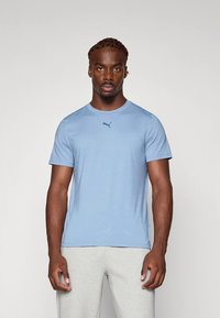 Camiseta deportiva azul claro hecha de tela transpirable, con cuello redondo y un pequeño logotipo de Puma en azul marino en el pecho.