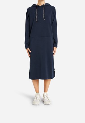 Abito felpa blu navy con lacci a contrasto, maniche lunghe, vestibilità comoda e fessure laterali, abbinato a sneakers sportive bianche.