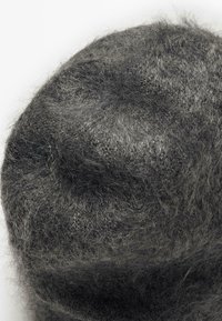 Berretto lavorato a maglia morbido e peloso di un grigio scuro con un leggero dettaglio rialzato sulla parte superiore, su uno sfondo bianco uniforme.