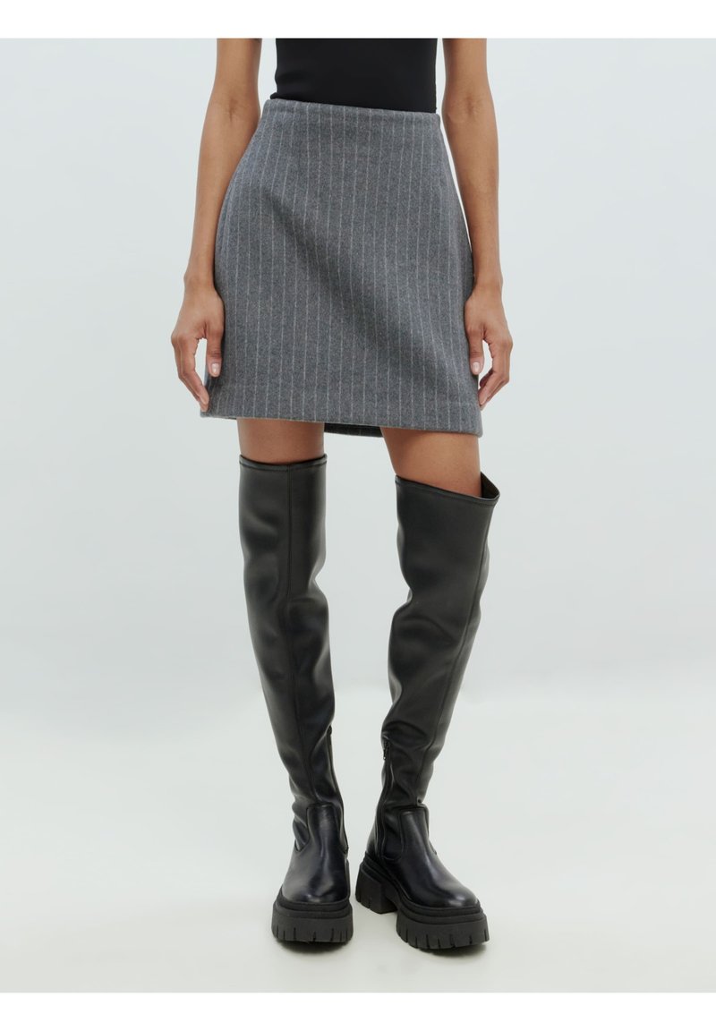 Mini-jupe grise à rayures faites d'un tissu texturé, associée à des bottes noires en cuir montant jusqu'aux genoux avec une semelle épaisse et une finition lisse.