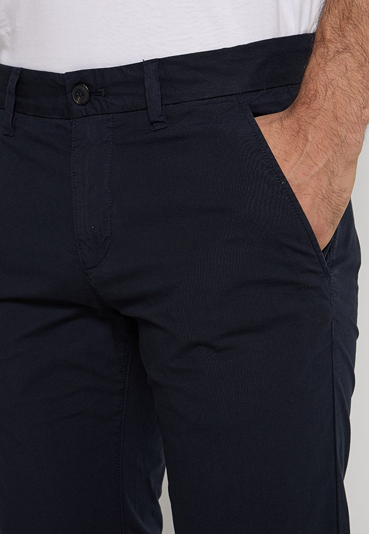 Granatowe chino wykonane z miękkiej mieszanki bawełny, charakteryzujące się slim fit, przednimi kieszeniami oraz pojedynczym zapięciem na guzik w talii.