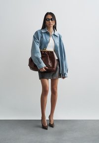 Denim jacket with a light wash and oversized fit, white ribbed top, gray suede skirt, brown leather handbag, and pointy brown heels.