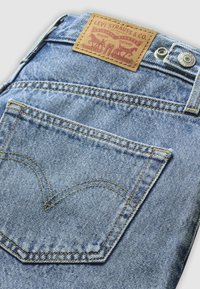Baglomme på lyseblå Levi's jeans med gul syning, metal knap og brun læder mærke med to heste og tekst.