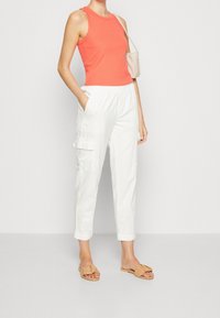 Koraalribbed tanktop, witte cargo broek met zijzakken en beige instapsandalen. Glad textiel met een casual pasvorm.
