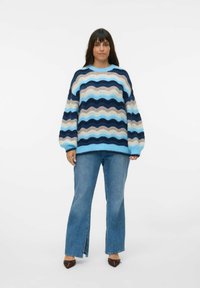 Kleurrijke gebreide trui met golvende blauwe, beige en marineblauwe strepen, met een losse fit, ronde hals en geribde manchetten. In combinatie met uitlopende jeans.