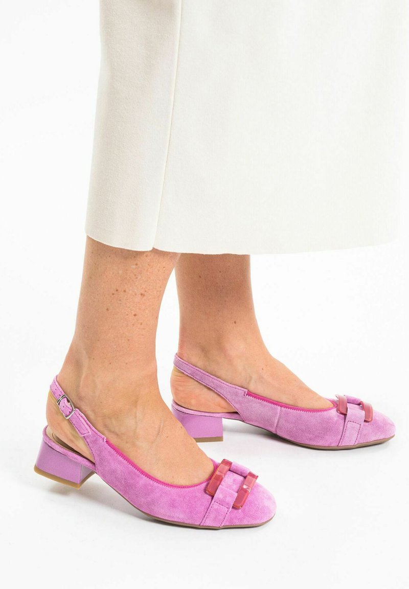 Scarpe slingback in suede rosa con tacco a bloco e fiocco decorativo. La fascia presenta una fibbia e la punta è arrotondata con una trama liscia.