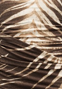 Καφέ και μπεζ ύφασμα με αφηρημένα γεωμετρικά και ζεβροειδή ρίγες, εμφανιζόμενο με πτυχές και ελαφρές παραλλαγές υφής.