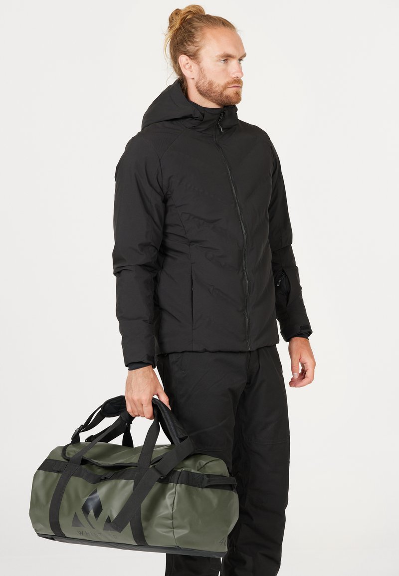 Musta eristetty takki huppuineen, joka sisältää etuvetoketjun ja sivutaskut. Henkilö pitää tummaa vihreää vedenpitävää urheilukassia.