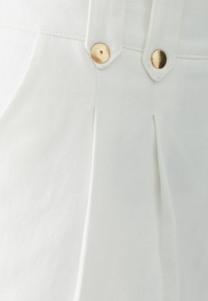 Pantaloni bianchi in cotone con pieghe frontali e bottoni in metallo dorato. Il tessuto presenta una sottile texture, enfatizzando un aspetto pulito e ben rifinito.