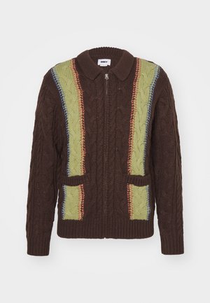 Brun strikket cardigan med lynlås, med grønne og flerfarvede kabelmønstre samt to forlommer. Design med rund krave.