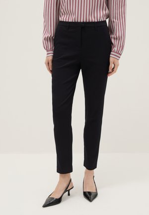 Mujer con pantalones ajustados negros hasta el tobillo combinados con tacones slingback negros de punta fina y una blusa de manga larga a rayas rojas.