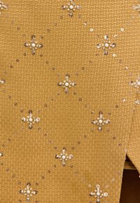 Textil en amarillo mostaza con un tejido texturizado, adornado con lentejuelas y cuentas dispuestas en patrones florales por toda la tela.