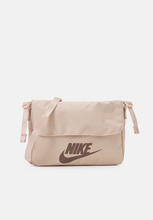 Sac bandoulière Nike beige avec sangle ajustable et fermeture à rabat, arborant le logo Nike en marron foncé sur le devant.